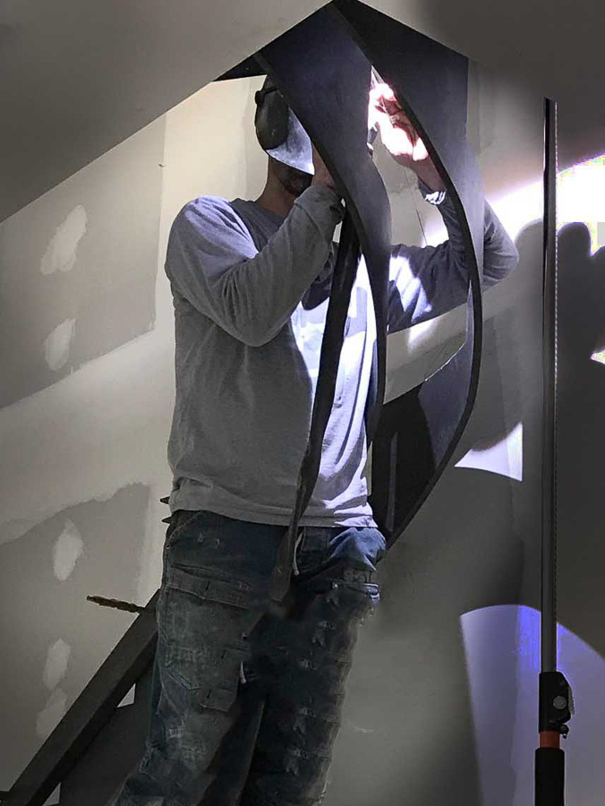 Un artisan métallier de notre atelier près de Lyon, travaillant avec soin sur un escalier métallique à limon décalé sur mesure, destiné à une résidence située dans une commune limitrophe du département du Rhône.