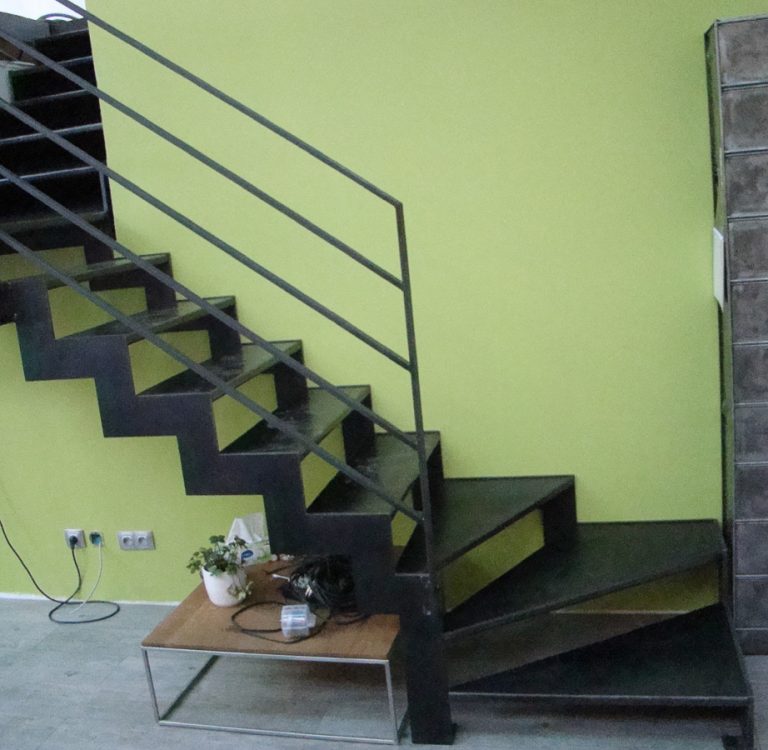 Escalier métallique noir sur mesure, réalisé avec grande finesse par un artisan talentueux basé à Lyon dans le Rhône, contrastant de manière élégante avec les murs verts de la pièce.