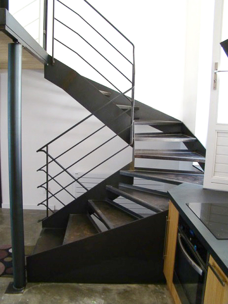 Un escalier en spirale métallique sur mesure, conçu et fabriqué avec une grande qualité par notre artisan métallier basé à Lyon, dans le département du Rhône, comme élément distinctif d'une cuisine.