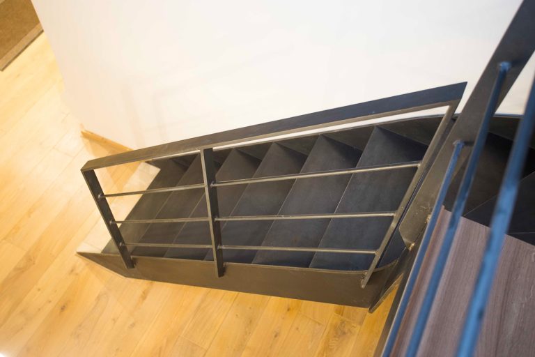 Escalier métallique sur mesure avec une balustrade noire et un sol en bois, réalisé par un artisan métallier de grande qualité basé à Lyon, dans le département du Rhône.