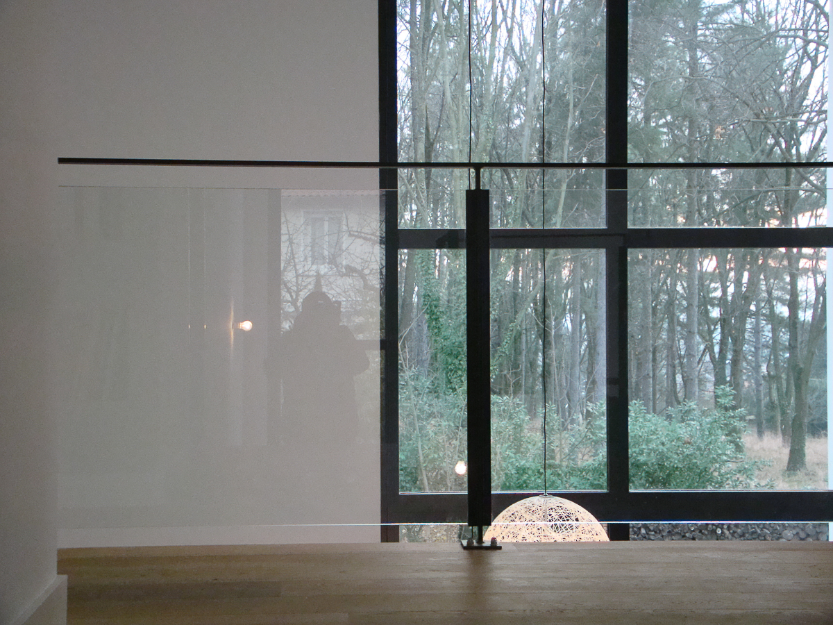 Une balustrade en verre dans une pièce avec vue sur les bois.