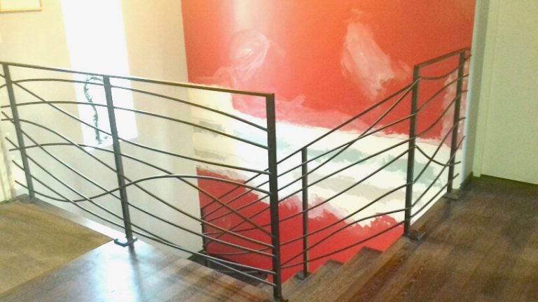 Un escalier avec une rampe en métal et un mur rouge.