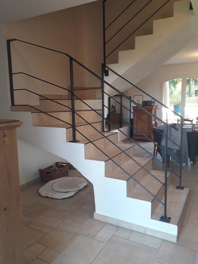 Un escalier dans une maison avec une rampe noire.