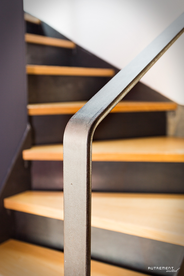 Une rampe métallique sur un escalier en bois.