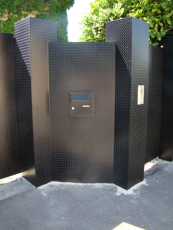 Une clôture métallique avec une boîte aux lettres au milieu.