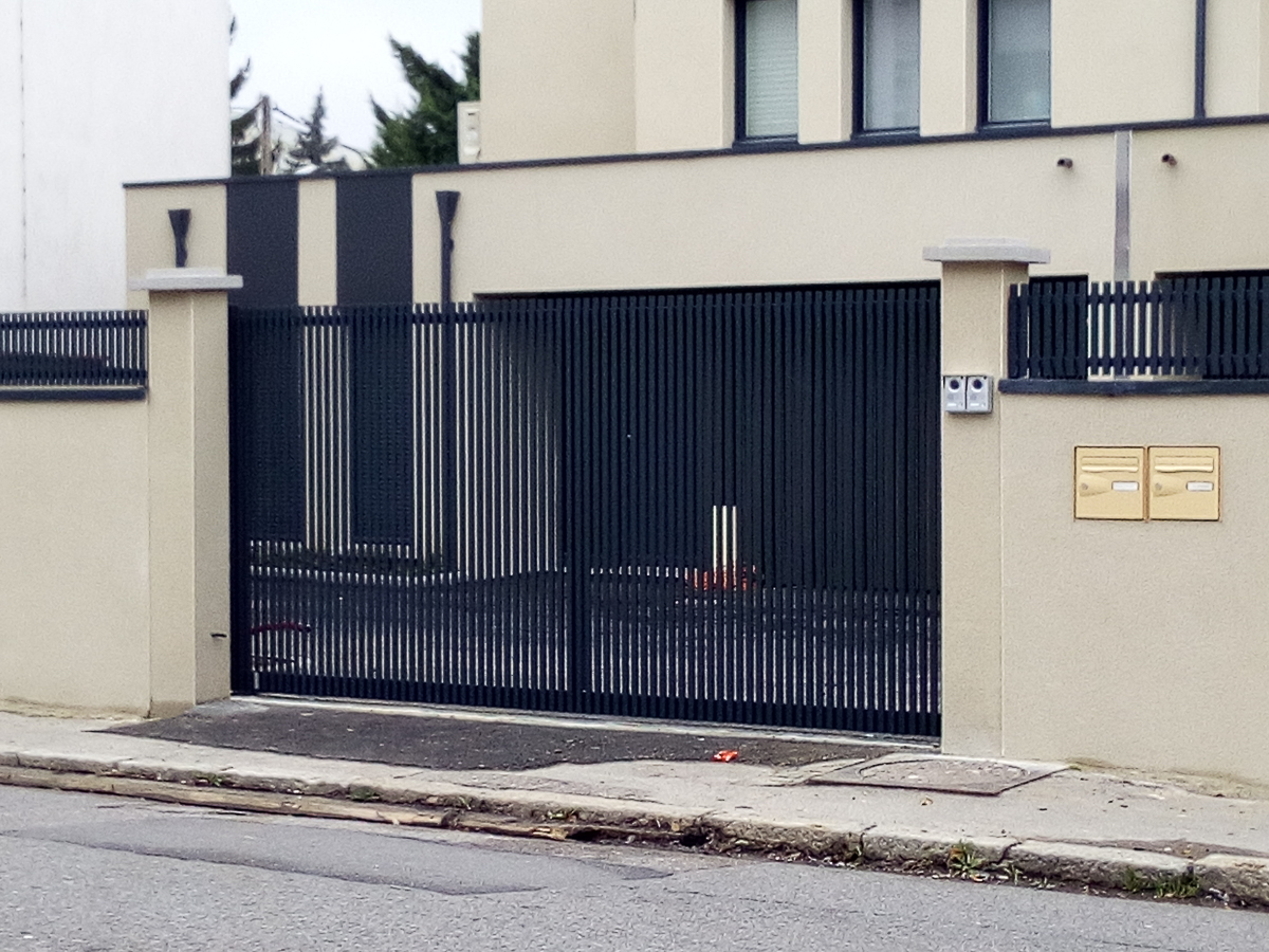 Un portail métallique devant une maison dans une rue.