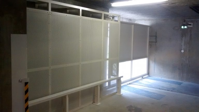 Un mur blanc avec une porte métallique au milieu.