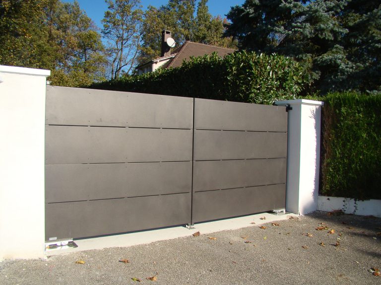 Un portail en métal avec une clôture blanche devant.