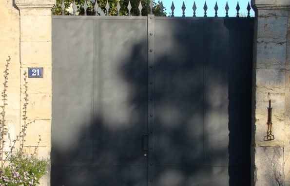 Un portail en métal noir devant un bâtiment en pierre.