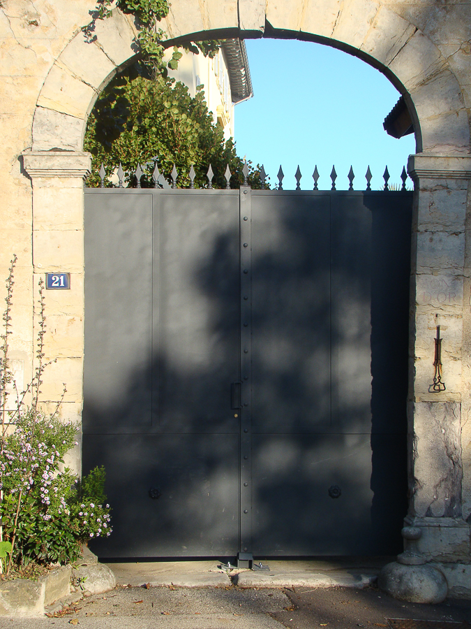 Un portail en métal noir devant un bâtiment en pierre.