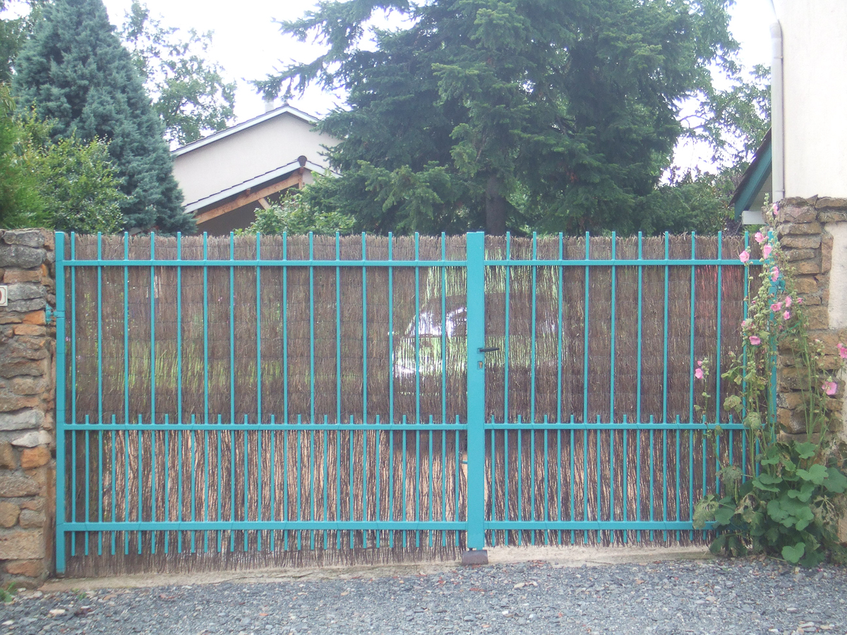 Un portail métallique avec un mur de pierre devant une maison.