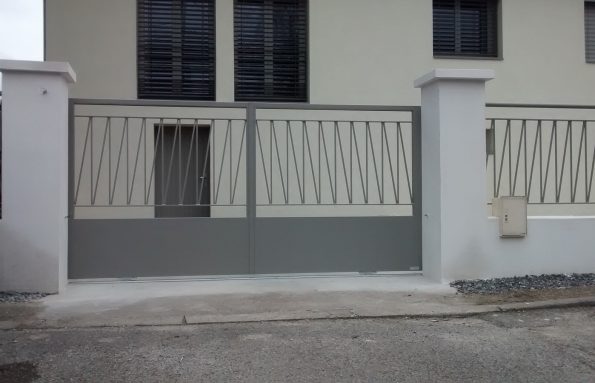 Une balustrade métallique entoure un portail blanc devant une maison.