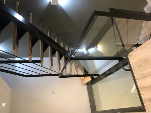 Un escalier avec des rampes en verre et un plancher en bois, avec des accents métalliques.