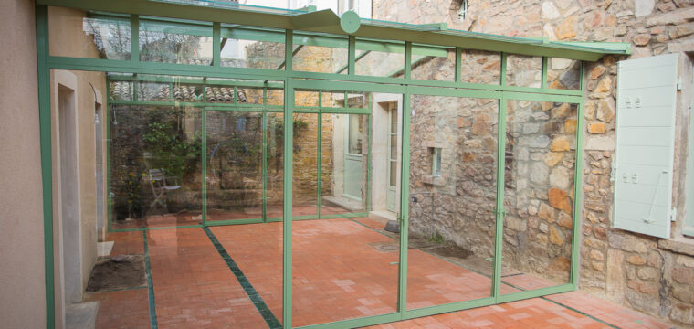 "Véranda sur mesure en verre vert à Lyon, accentuée par un mur de pierre."