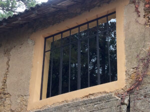 Une fenêtre en métal avec des barreaux en fer forgé sur un mur en pierre.