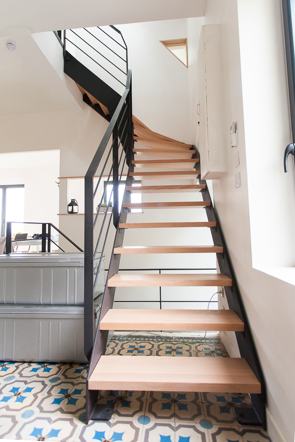 Escalier métallique réalisé sur mesure, remarquable de haute qualité par notre artisan métallier basé à Lyon dans le Rhône, se distinguant harmonieusement sur un plancher en carreaux bleus d'une maison lyonnaise.