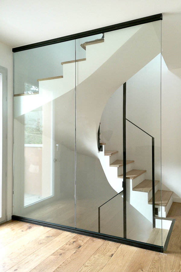 Un escalier en verre et métal dans une pièce avec parquet en bois franc.