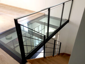 Un escalier en verre dans une maison avec un plancher en bois, orné d'accents métalliques.