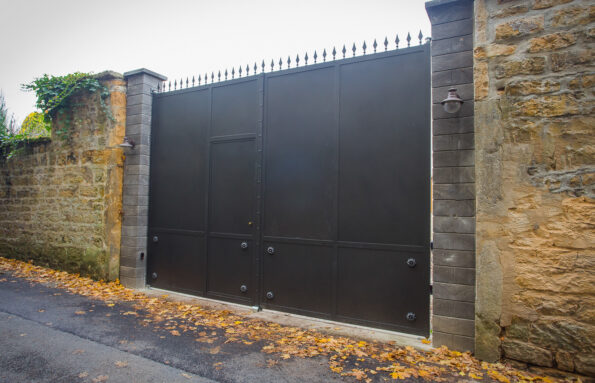Une porte noire en métal sur un mur de pierre.