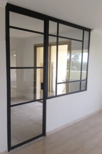 Une porte coulissante en verre noire en métal dans une pièce vide.