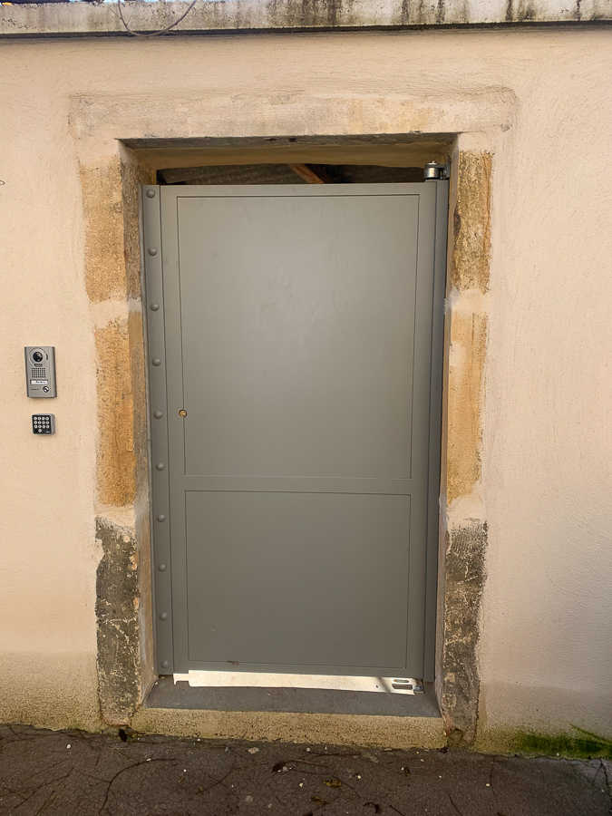 Une porte métallique se trouve à côté d’un mur de pierre.