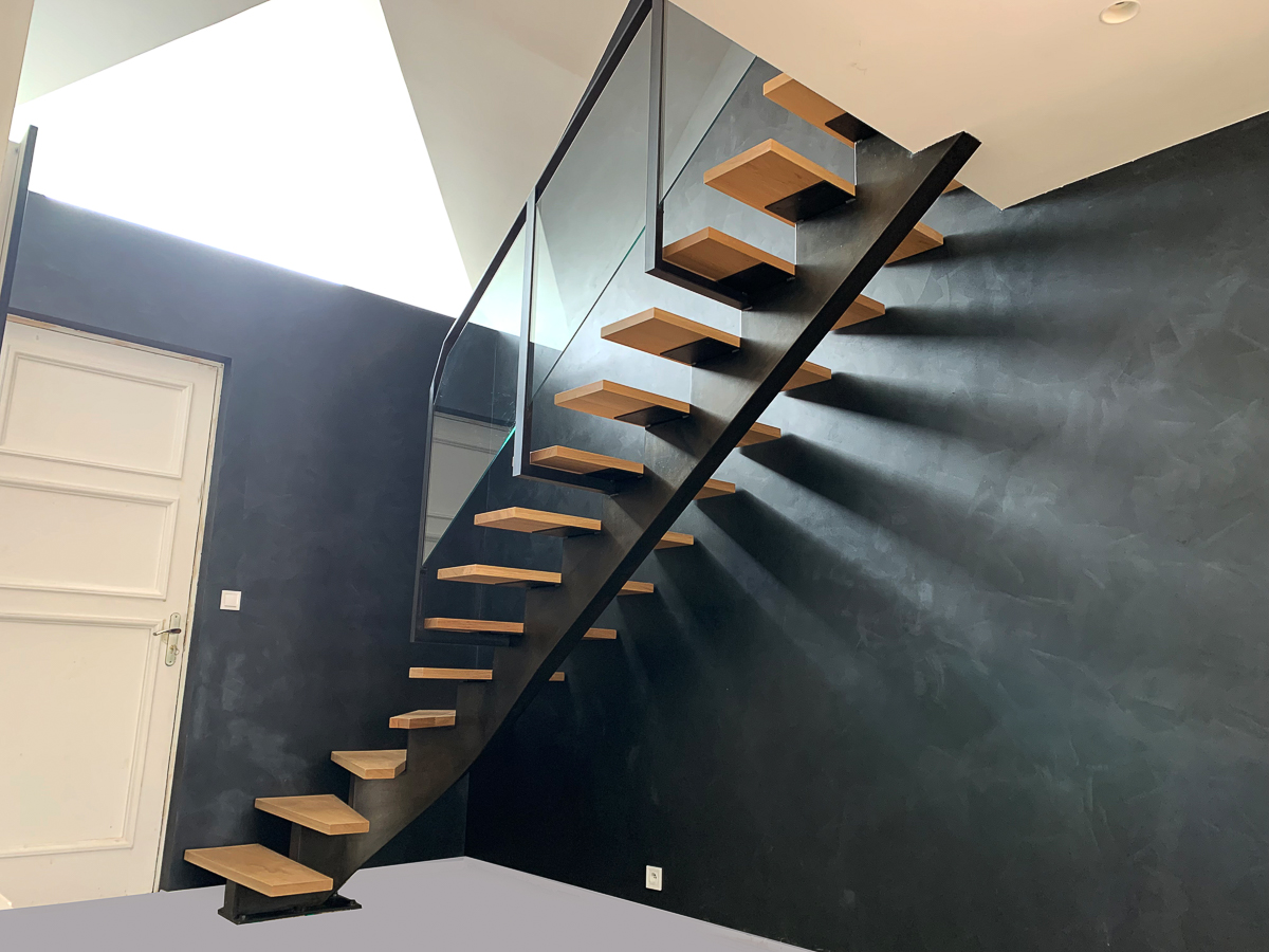 Un escalier métallique sur mesure de grande qualité, réalisé par un artisan métallier à Lyon dans le département du Rhône, dans une pièce dotée de murs noirs.