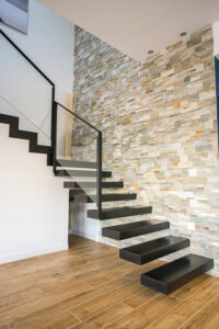 Un escalier moderne avec une rampe en métal noir et un mur en pierre.