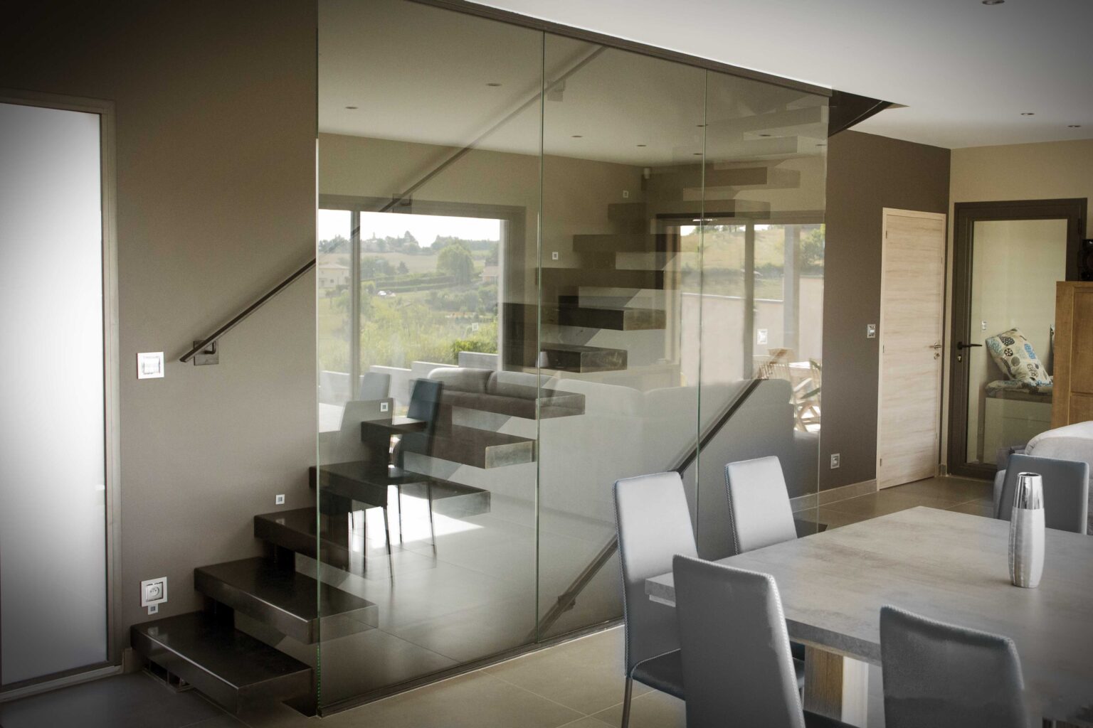 Salle à manger contemporaine dotée de murs en verre et d'un escalier suspendu.