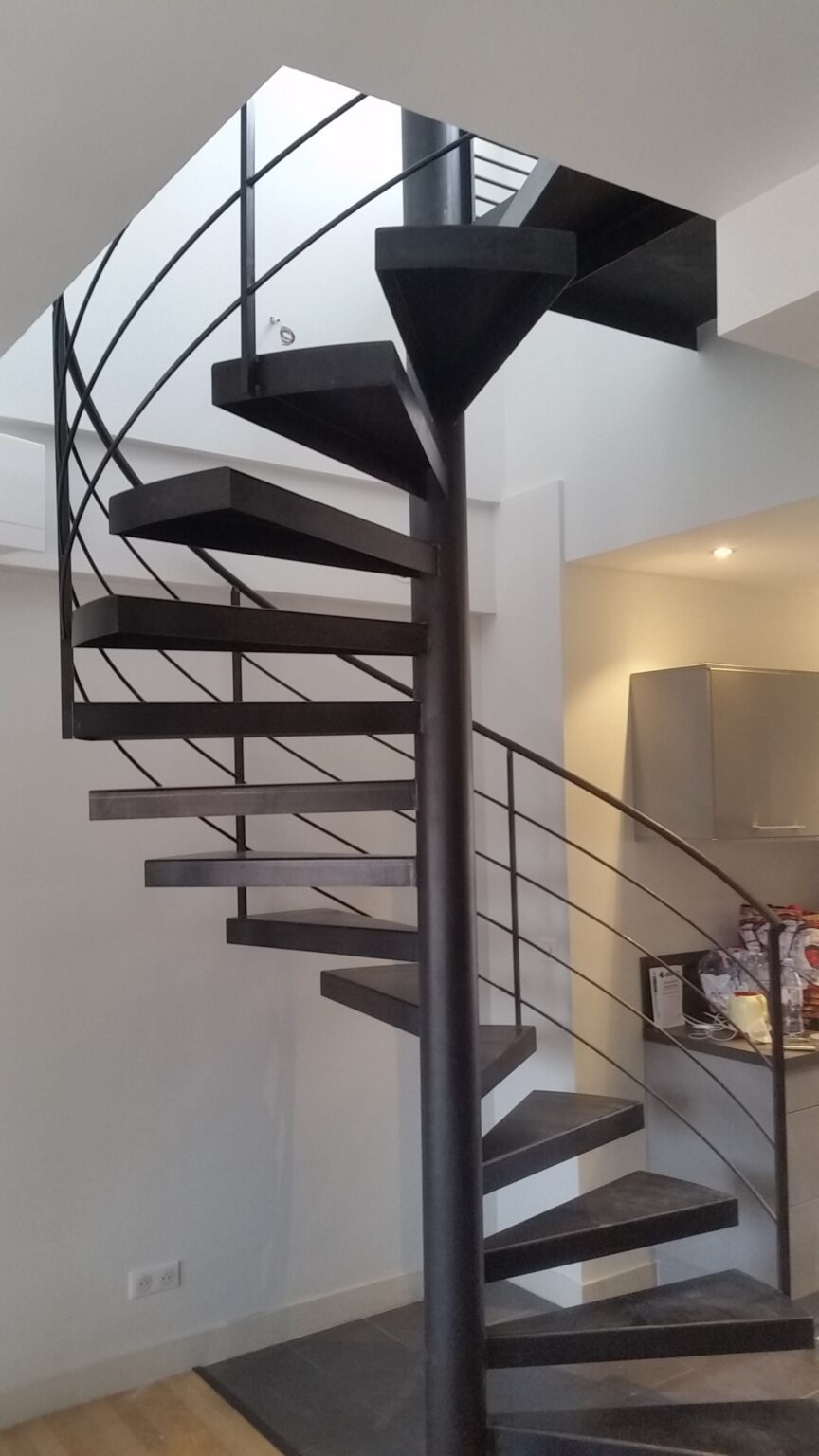 Escalier en spirale aux rampes métalliques noires situé dans un intérieur contemporain.