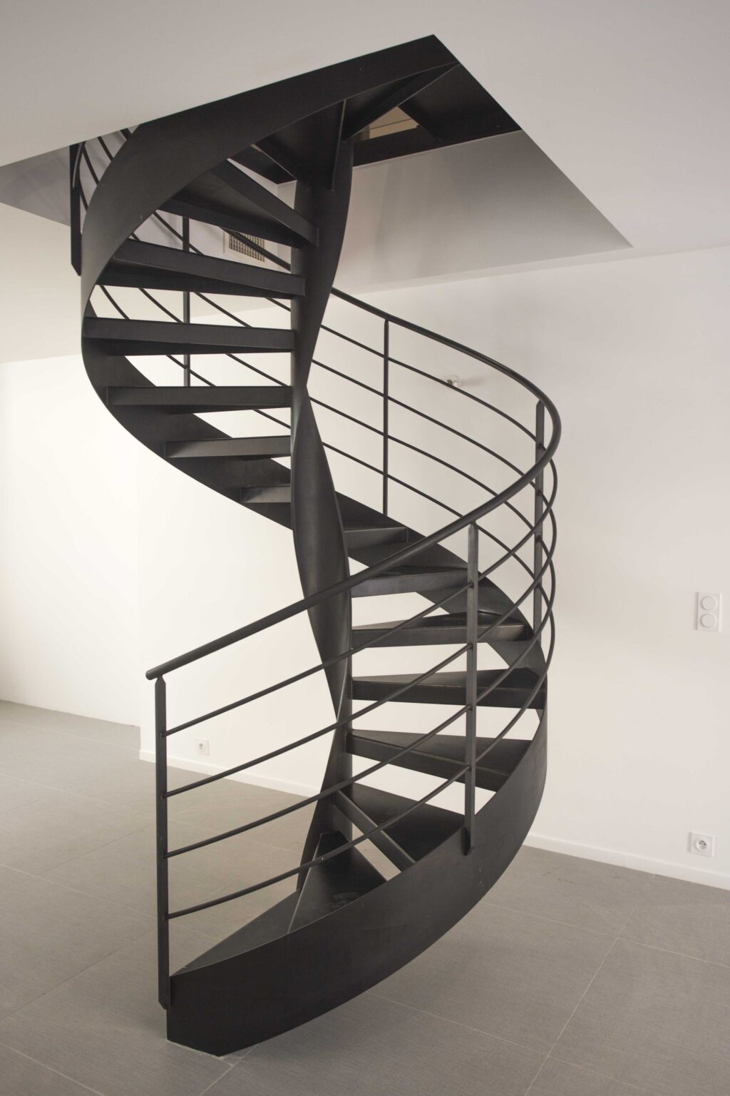 Un escalier en colimaçon moderne avec des rampes en métal noir dans un espace intérieur minimaliste blanc.