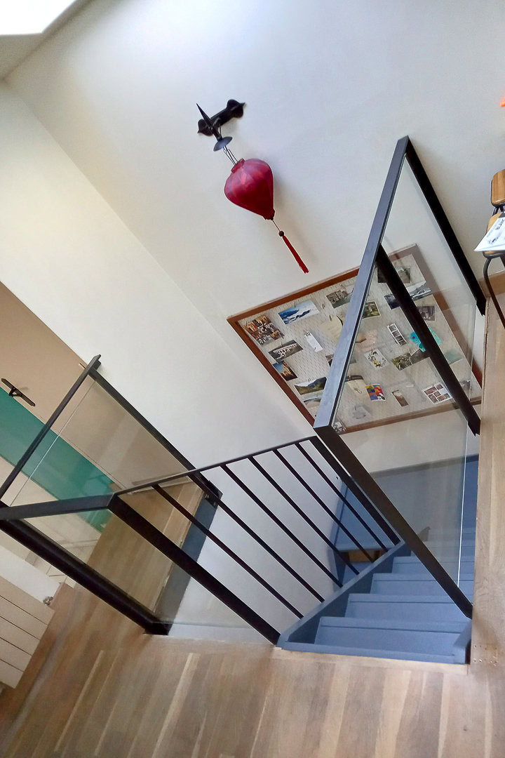 Un escalier moderne avec des rampes noires et des panneaux de verre comme garde-corps.