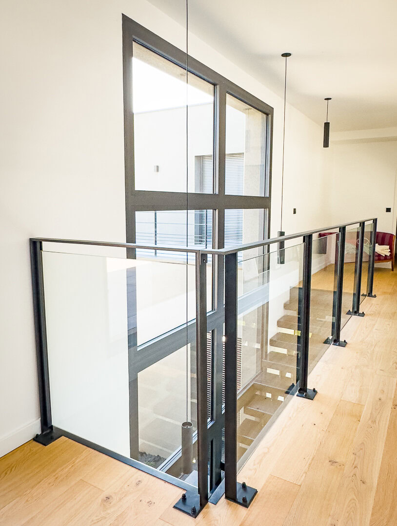 Un couloir moderne avec des garde-corps en verre et métal.