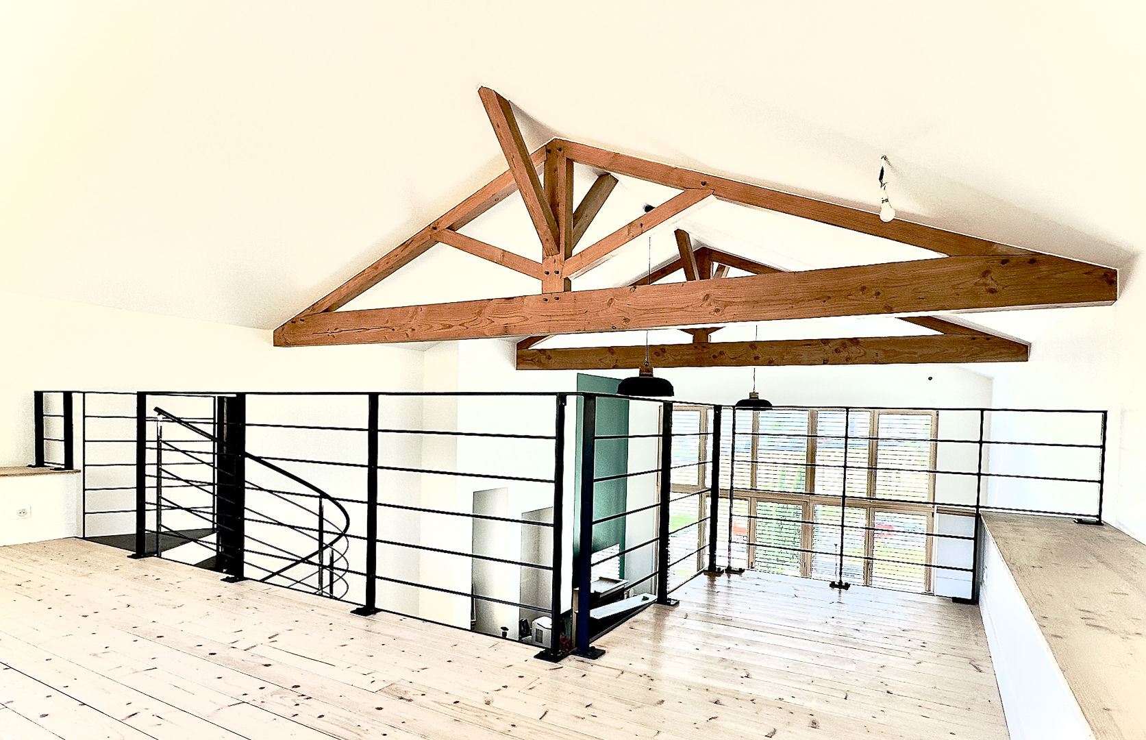 Loft contemporain avec poutres en bois, sol clair et rambarde en métal noir.