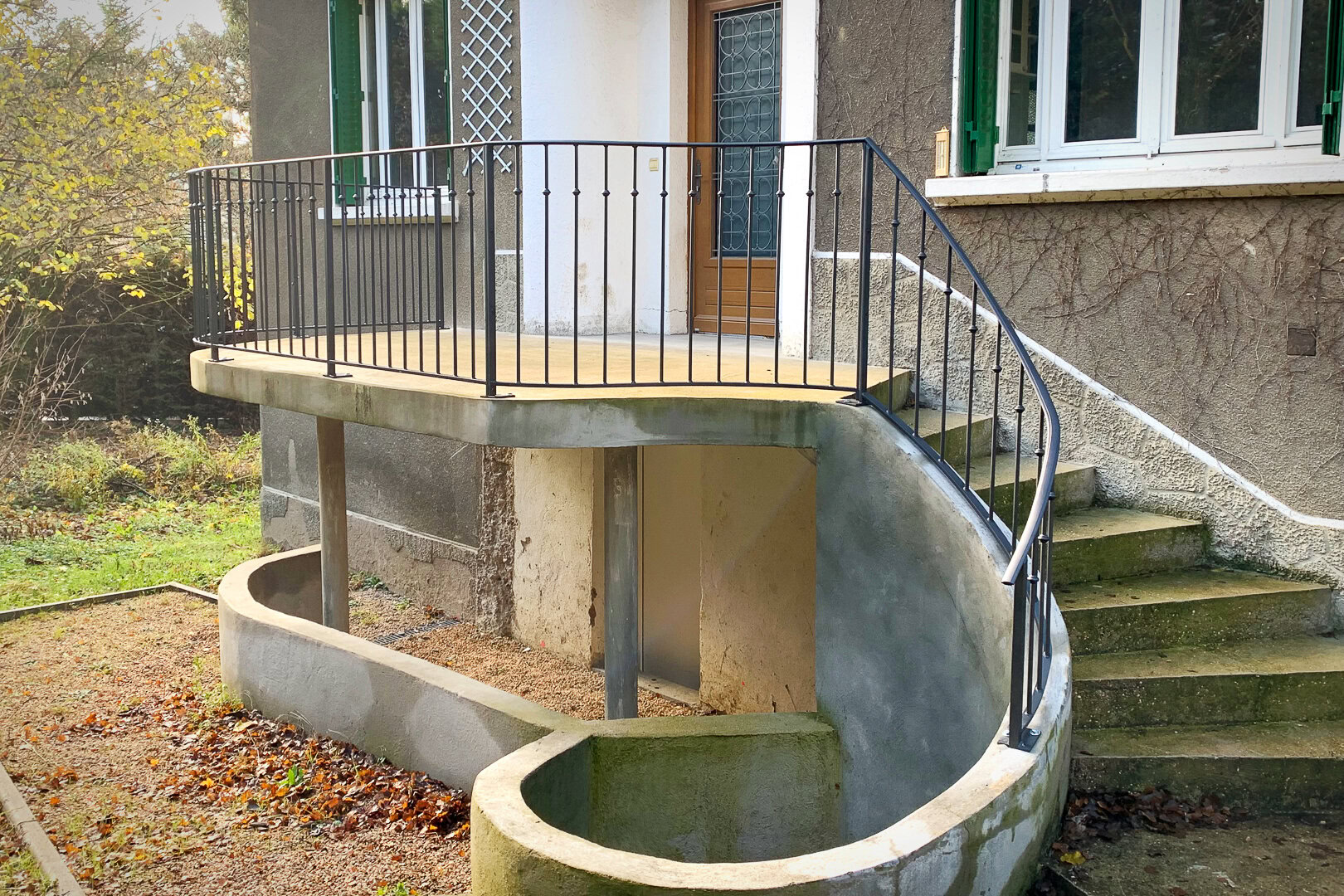 Un petit balcon avec une rambarde traditionnelle courbée mène à un escalier extérieur descendant vers le jardin de cette ravissante villa située aux abords de Lyon.