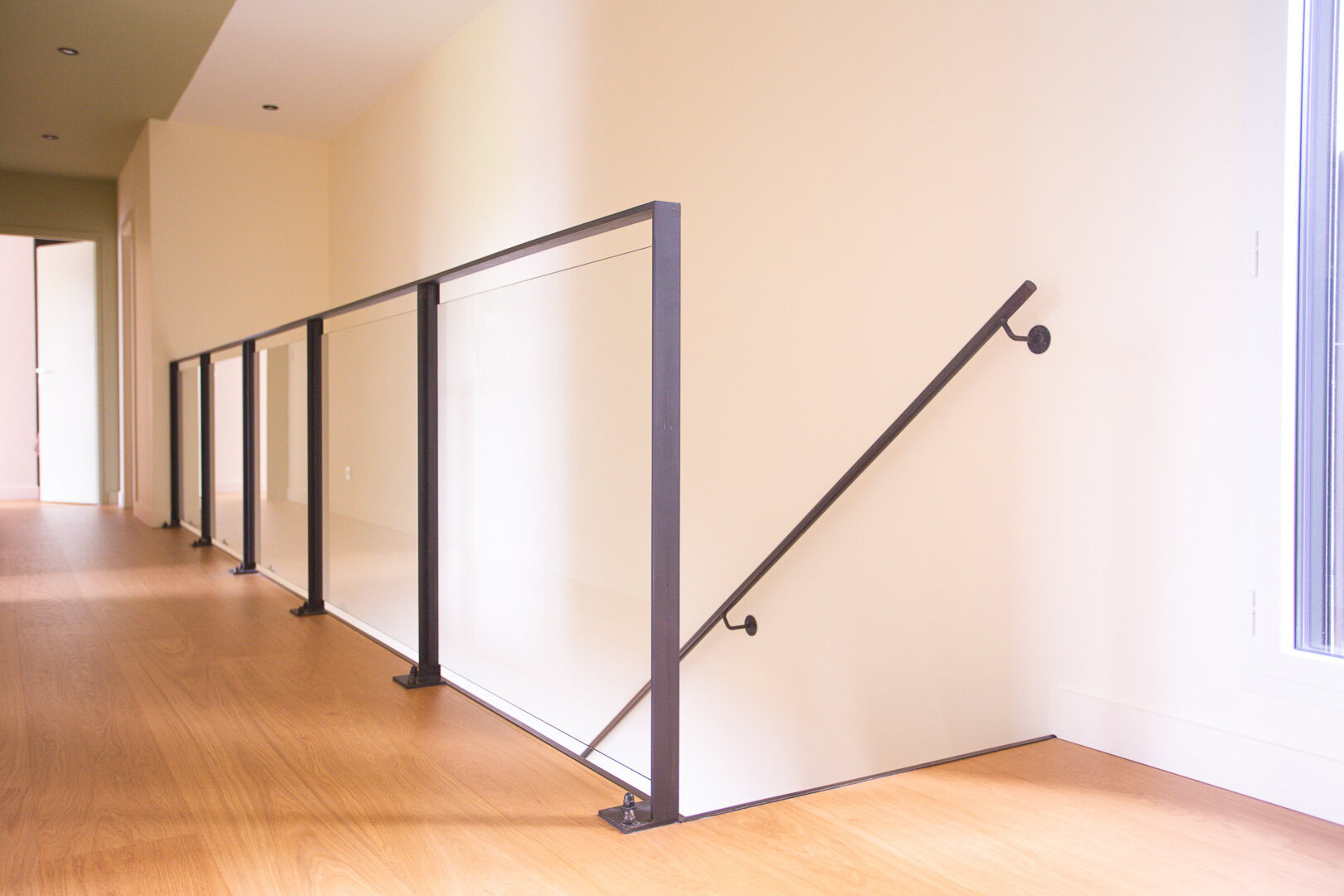 Escalier en métal avec garde-corps en verre et métal et main courante noire, conçu et posé par un métallier du Rhône.