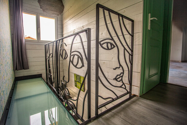 Rampe d'escalier en métal noir avec des dessins artistiques de visages, conçue et installée par un métallier du Rhône.