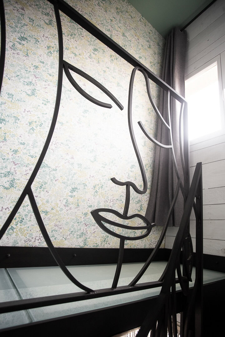 Un garde-corps en métal noir avec un dessin de visage abstrait, réalisé par un ferronnier d'art du Rhône près de Lyon.