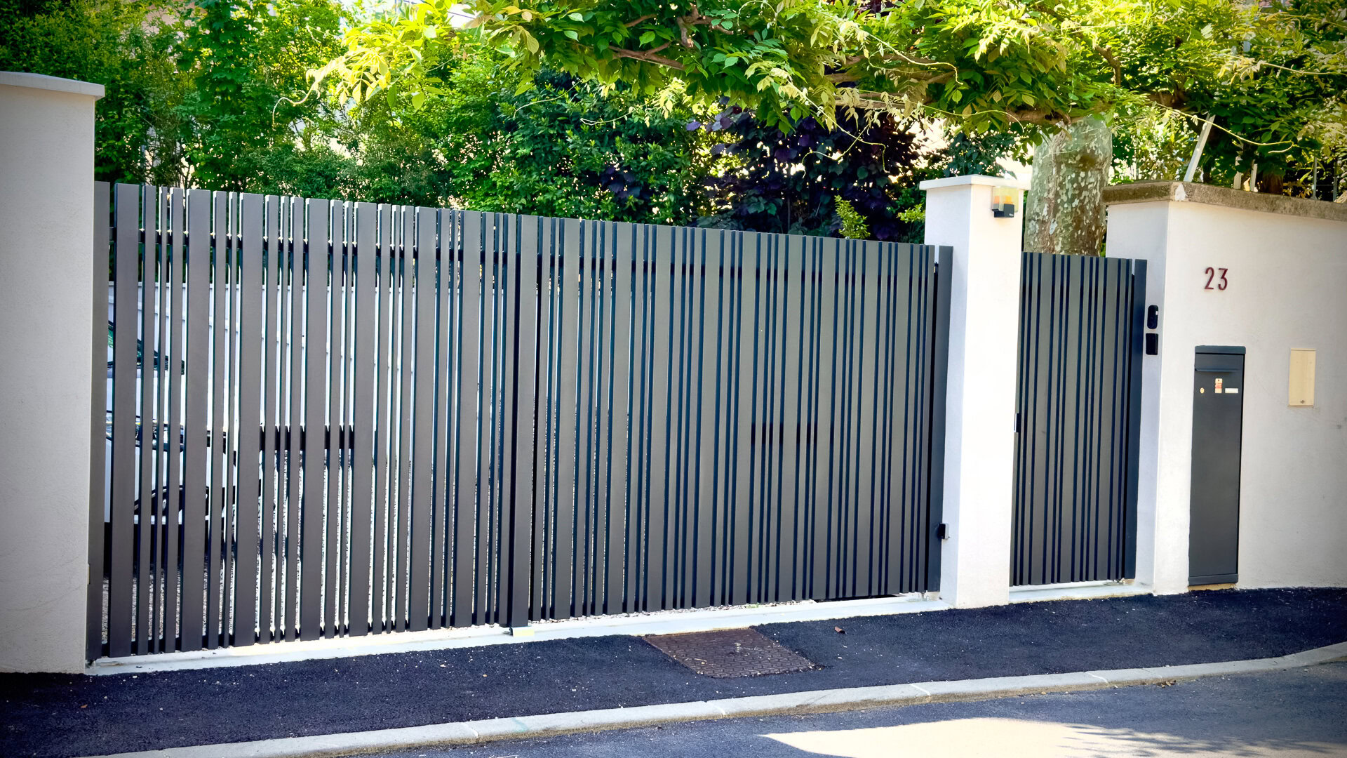 Portail moderne en métal à lattes, conçu et fabriqué sur mesure par un métallier près de Lyon, installé entre deux piliers blancs.
