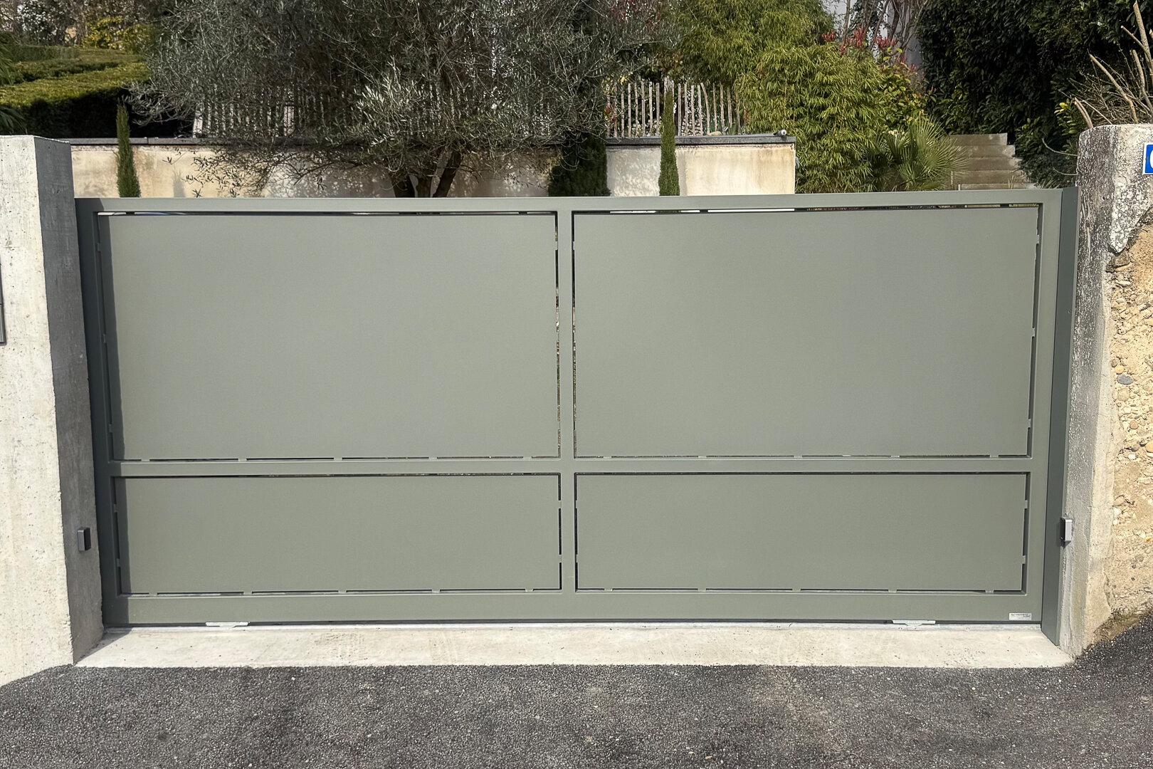 Portail moderne en métal gris fermé, conçu et posé par un métallier près de Lyon, séparant deux murs en béton.
