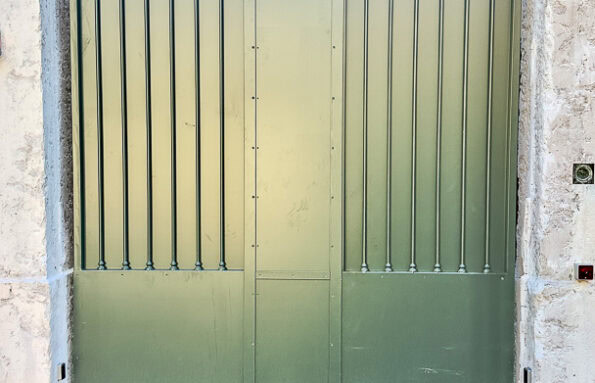 Portail en métal vert à barreaux verticaux, réalisé par un ferronnier d'art du Rhône, témoignant d'un travail de précision.