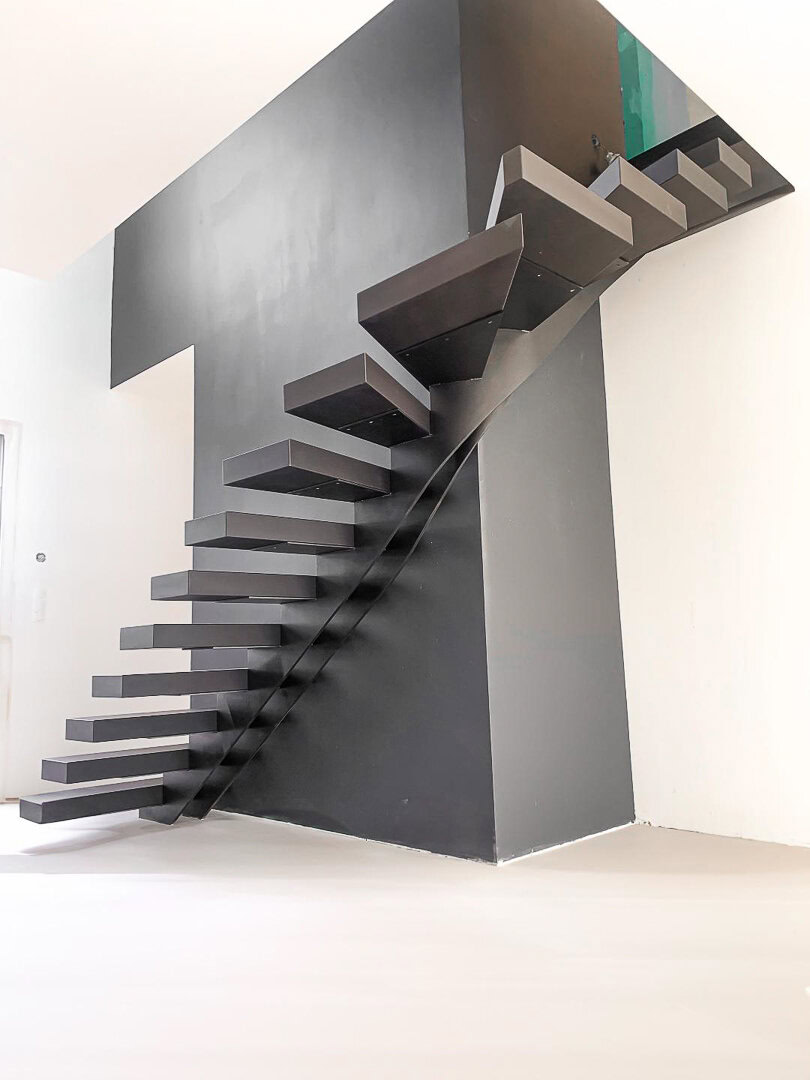 Un escalier flottant moderne aux marches épaisses et rectangulaires en métal noir, conçu et installé par un métallier du Rhône.