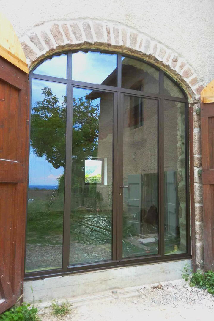 Verrière cintrée réalisée sur mesure, intégrée dans une arche en pierre.